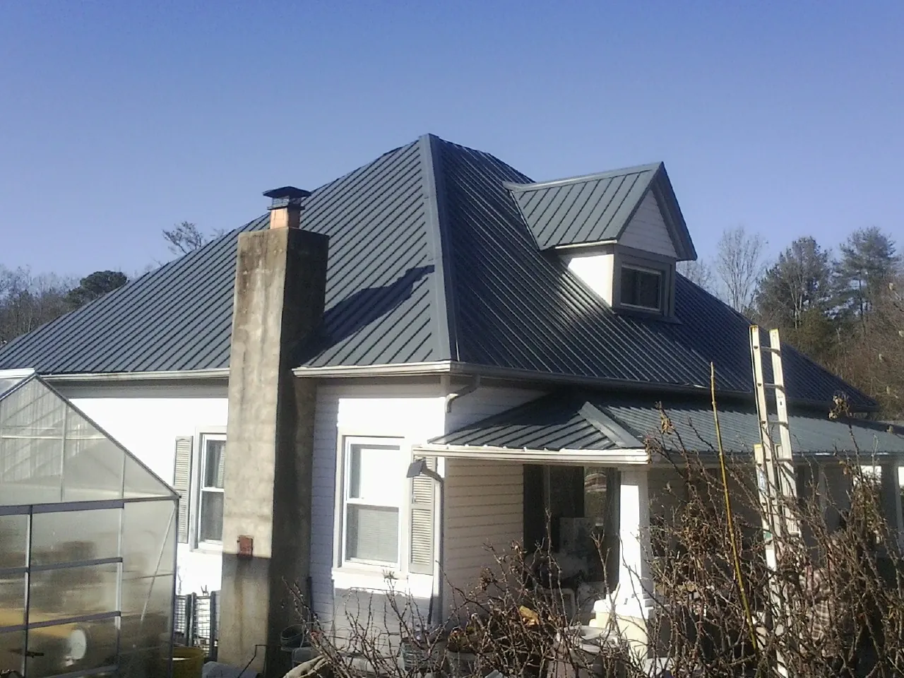 Dark blue standing seam metal roof on a white farmhouse with dormer — Slate & Tile Roof Repair by Roofing Brothers in Jenkinsville