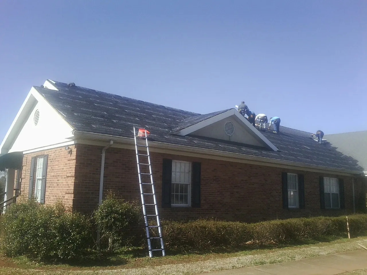 Crew tearing shingles off a brick ranch roof with a ladder set — Emergency Roof Repair work by our crew in Jenkinsville