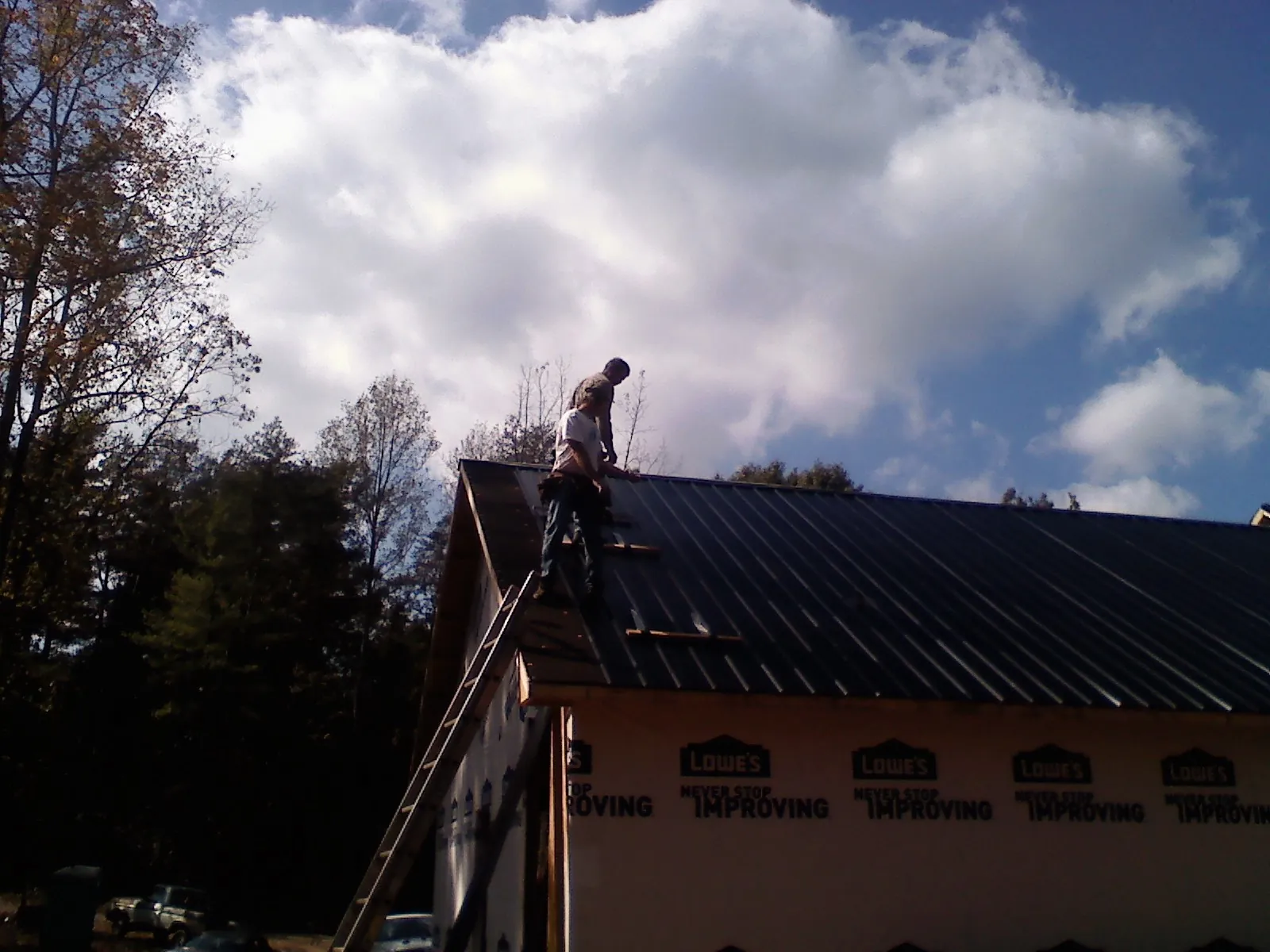 Roofer fastening dark metal panels high against a cloudy sky, from a Roof Inspection job in Jenkinsville