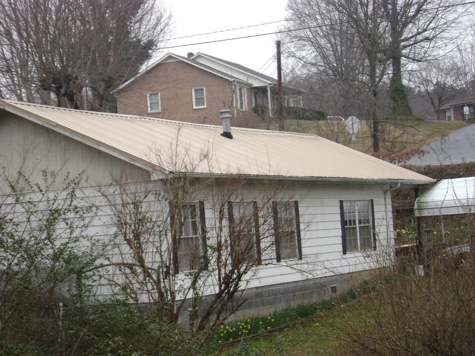 Tan metal roof on a white sided house set into a hillside — Commercial Roofing by Roofing Brothers in Jenkinsville